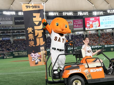 試合前、グラウンドにフラッグを持ったサトちゃんが登場